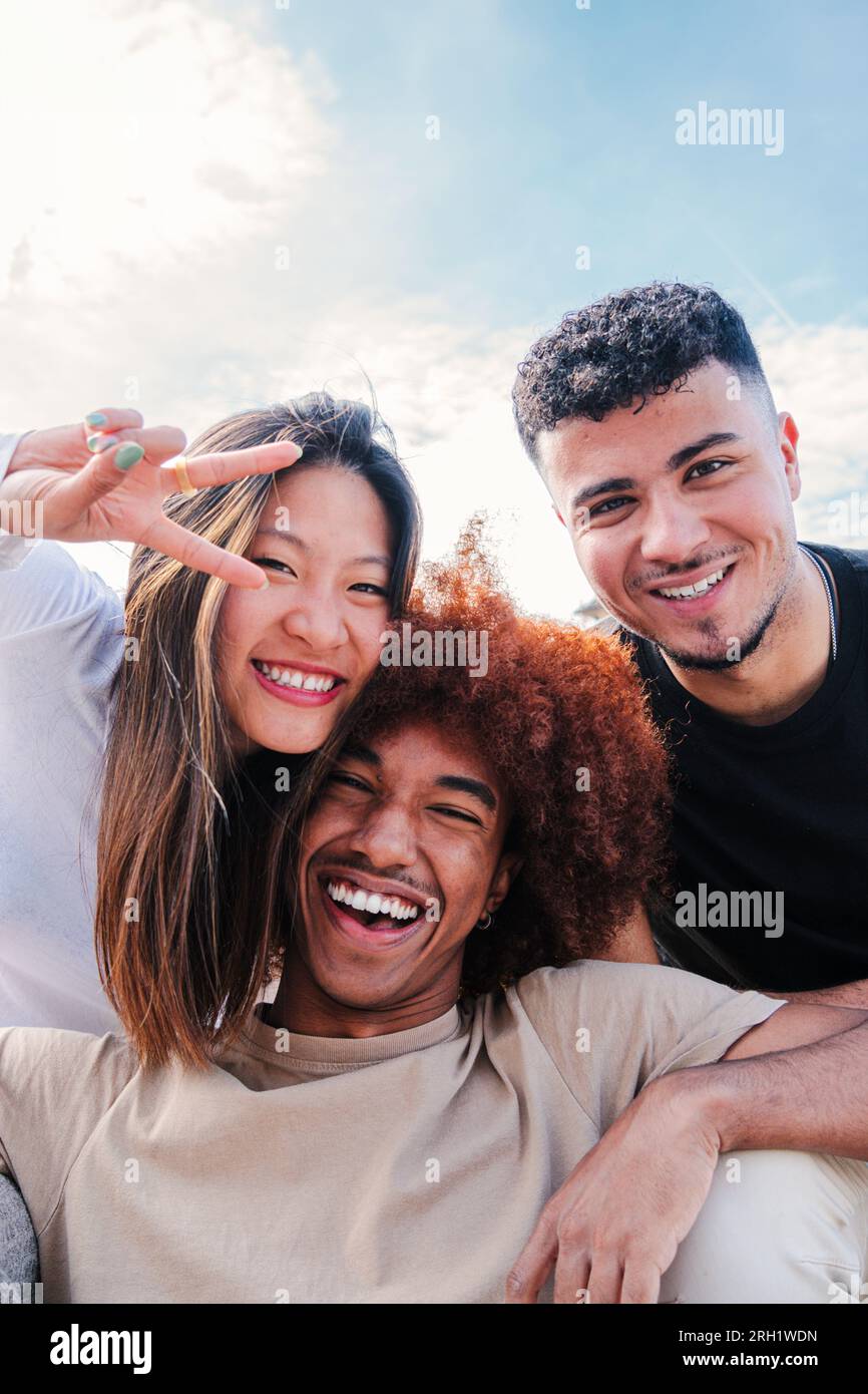 Portrait vertical d'un groupe de jeunes amis multiraciaux serrant et s'amusant ensemble. Trois copains cool heureux souriant regardant la caméra. Divers étudiants adolescents riant le lien le week-end. Photo de haute qualité Banque D'Images