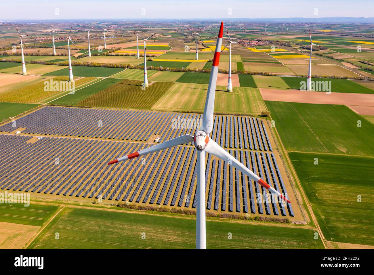 Vue rapprochée aérienne d’une éolienne devant des champs agricoles et des panneaux photovoltaïques d’un parc solaire en crise énergétique Banque D'Images