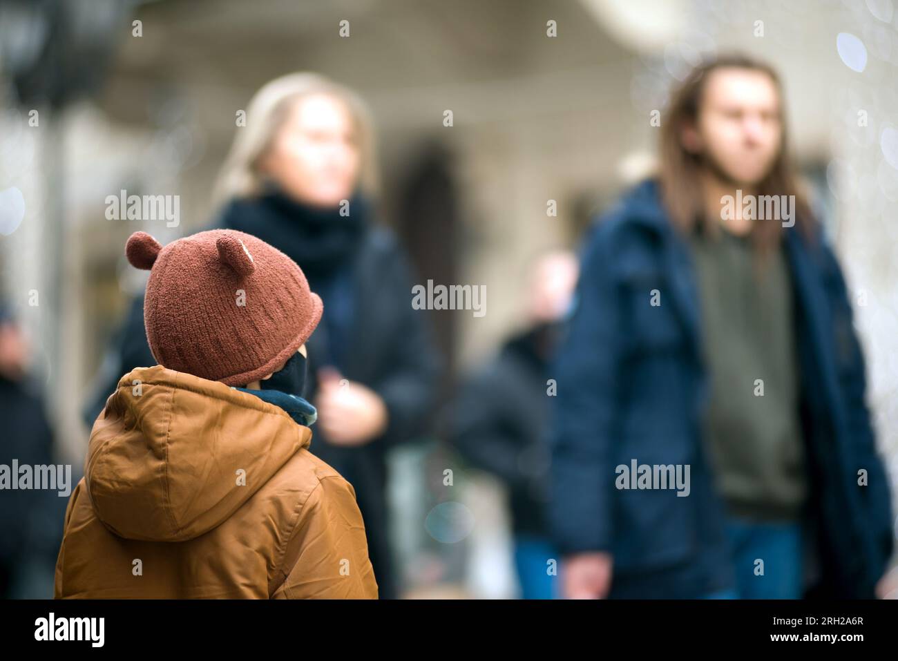 Enfant dans la rue regardant les gens défocalisés qui passent Banque D'Images