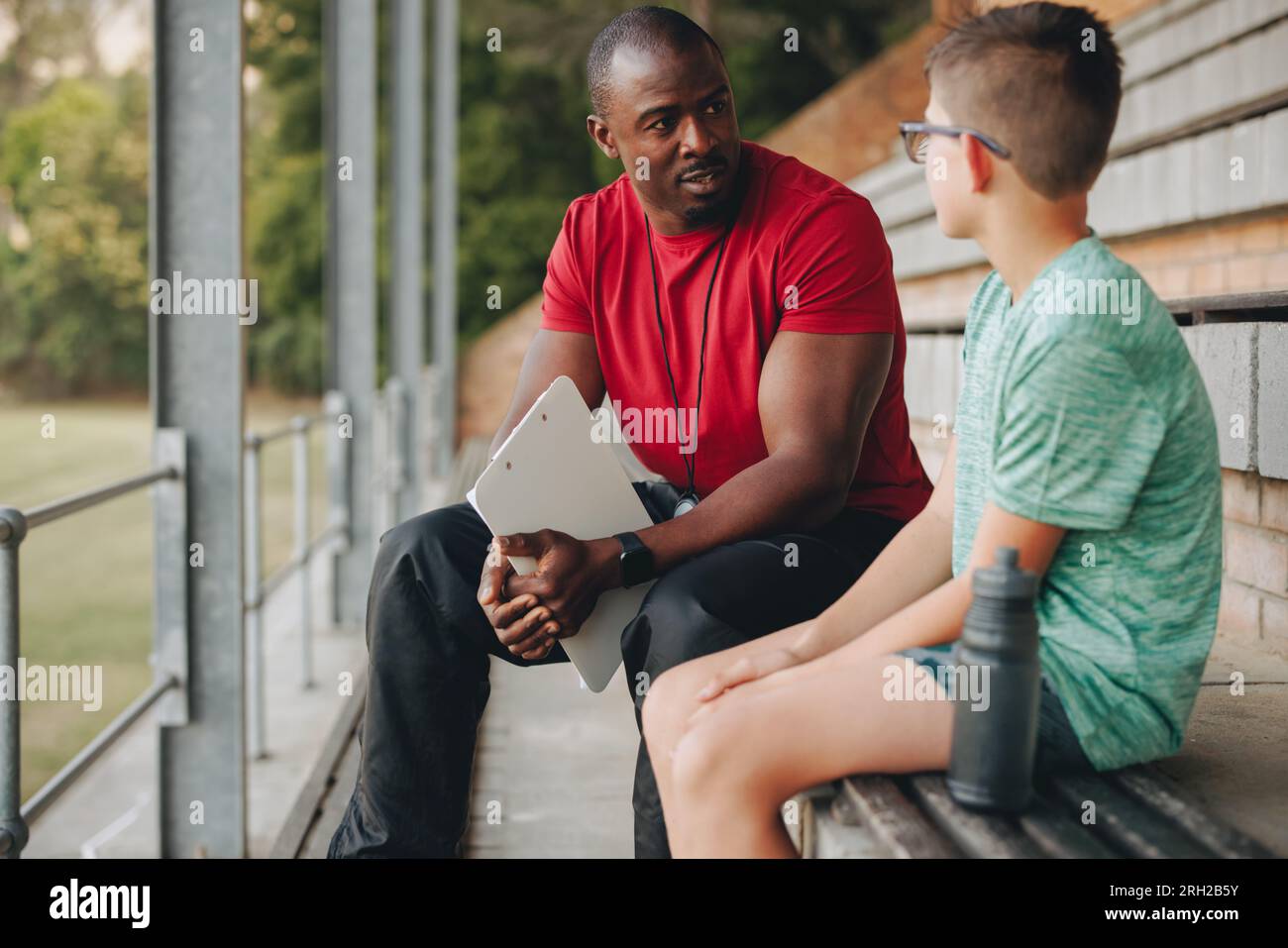 Entraîneur sportif parlant à un jeune garçon dehors à l'école primaire. Professeur masculin d'éducation physique motivant un jeune élève à l'école primaire. Enfant Banque D'Images
