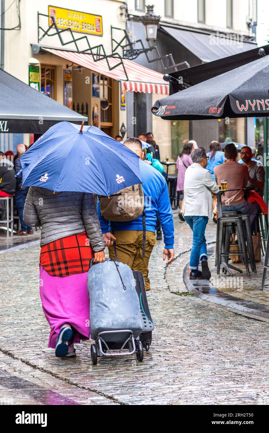 Couple avec bagages à roulettes marchant le long de la rue de la ville sous eparapluie pendant la pluie - Bruxelles, Belgique. Banque D'Images