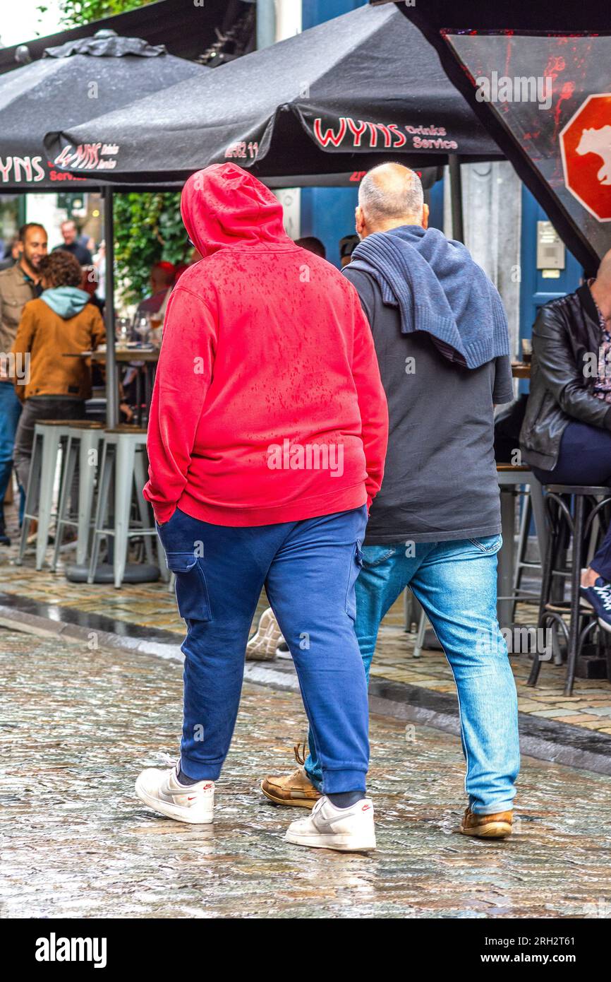 Deux hommes, un en sweat à capuche rouge, marchant le long de la rue de la ville - Bruxelles, Belgique. Banque D'Images