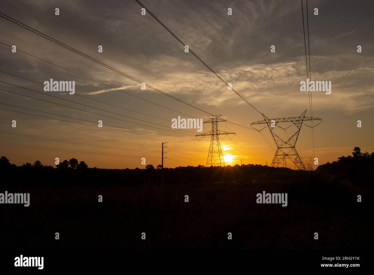 Le soleil se levant derrière une paire de grands pylônes électriques Banque D'Images