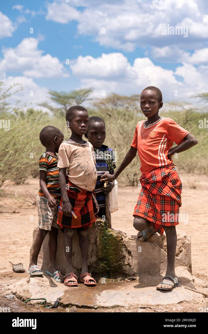 De jeunes garçons kenyans se tiennent près d'un robinet d'eau pour se procurer de l'eau douce à partir d'un trou de forage voisin, dans le comté de Baringo, au Kenya Banque D'Images
