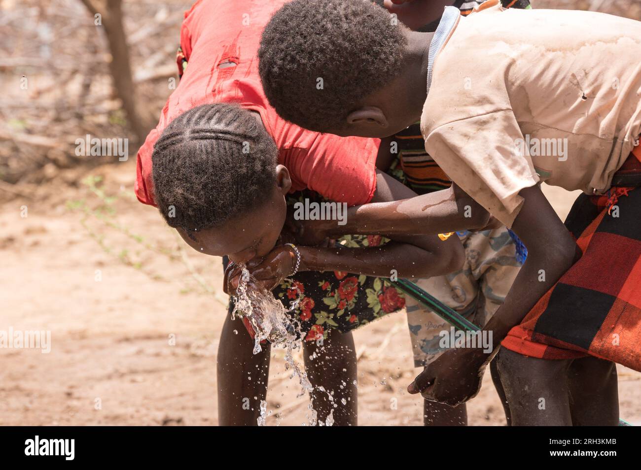 De jeunes enfants kenyans qui boivent à tour de rôle dans un tuyau d'eau douce avec de l'eau provenant d'un trou de forage voisin, dans le comté de Baringo, au Kenya Banque D'Images