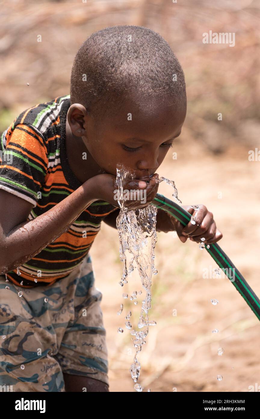 Un jeune garçon kenyan boit de l'eau fraîche dans une tubulure avec de l'eau provenant d'un trou de forage voisin, dans le comté de Baringo, au Kenya Banque D'Images