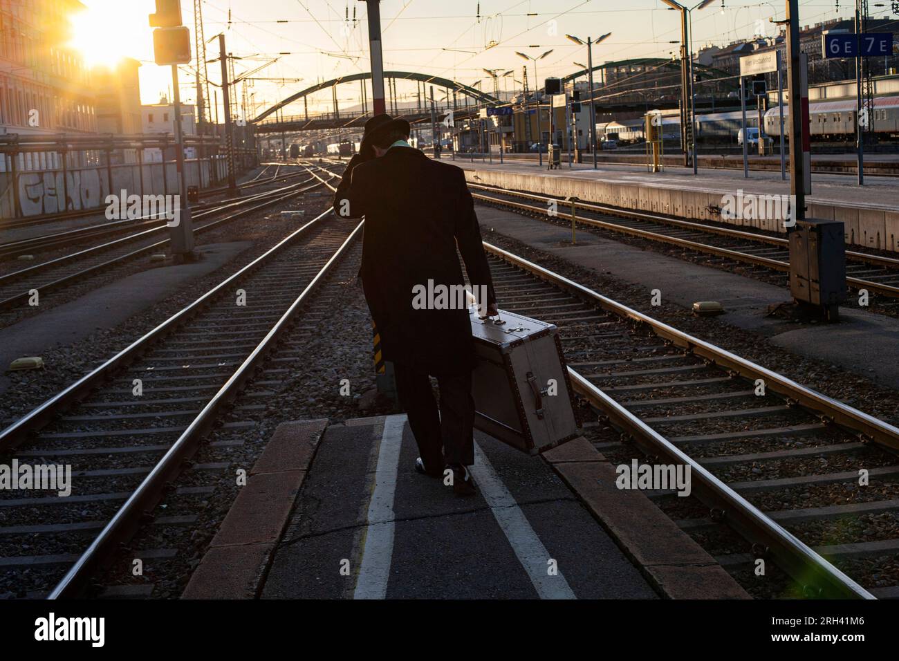 Un homme avec une valise marche à l'extrémité des racks de station de plate-forme tôt le matin Banque D'Images