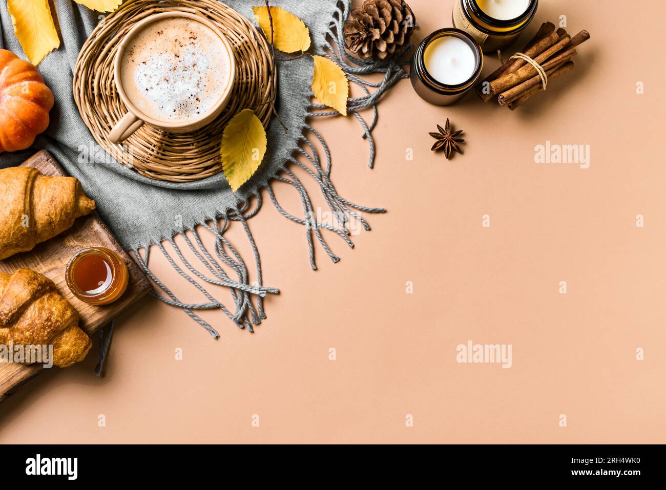 Concept esthétique d'automne. Tasse de café latte aux épices de citrouille, croissants, bougies, citrouille et feuilles d'automne jaunes sur fond beige, espace de copie. Banque D'Images