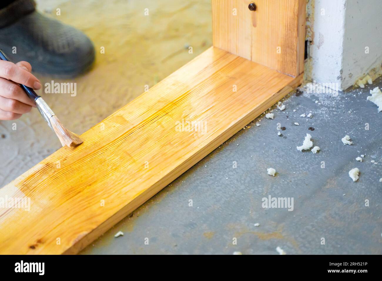 La main d'une femme avec un pinceau applique du vernis sur un seuil en bois d'une porte, gros plan. Protection contre l'humidité des pièces de pin dans la maison. Fait à la main dans un p Banque D'Images