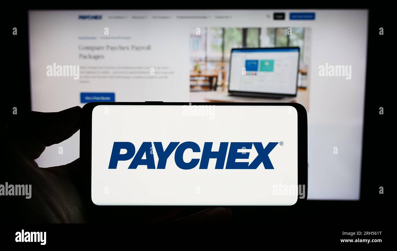 Personne tenant le téléphone portable avec le logo de la société d'externalisation américaine Paychex Inc. Sur l'écran devant la page Web d'affaires. Concentrez-vous sur l'affichage du téléphone. Banque D'Images