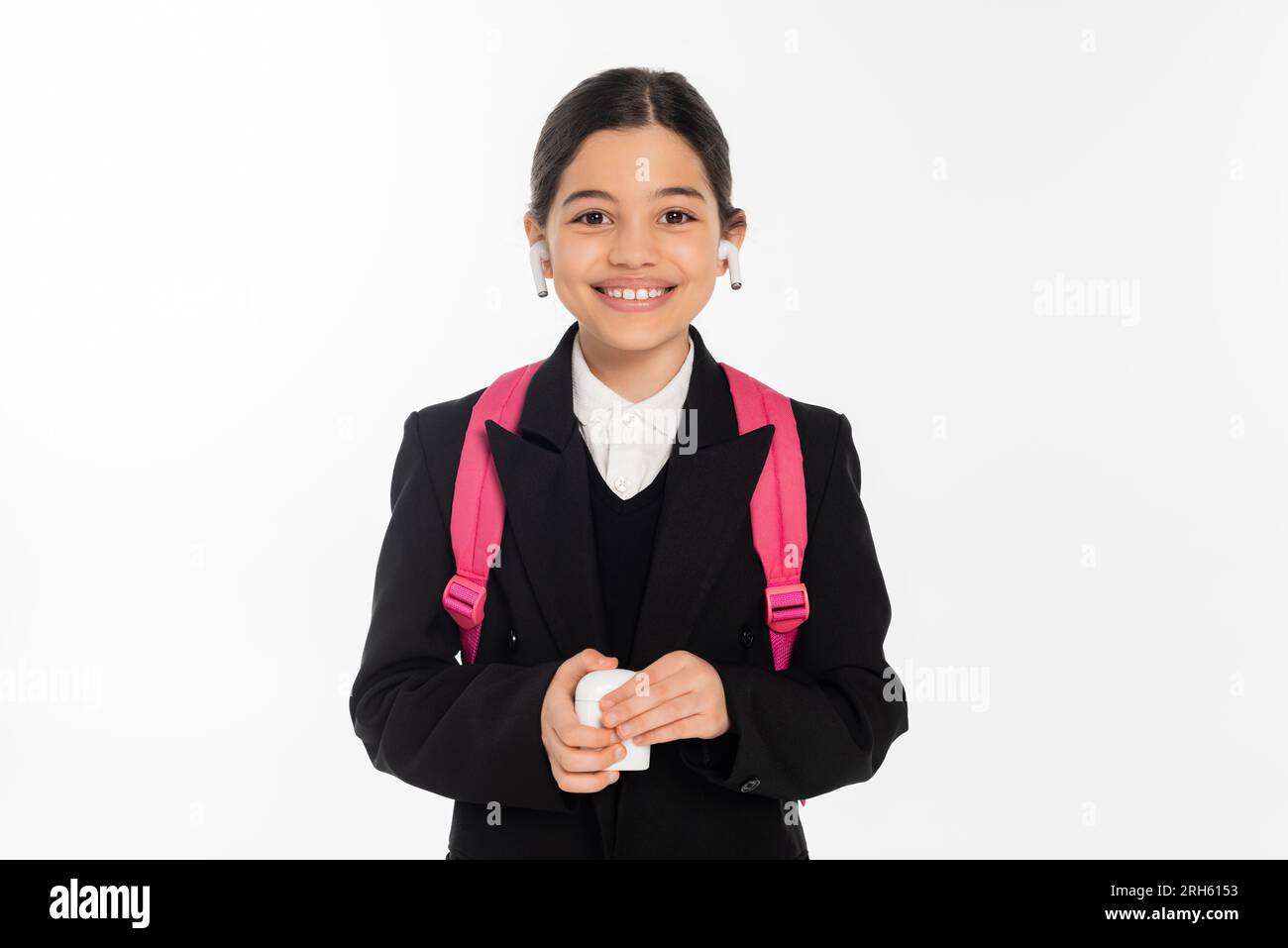 écolière souriante dans un étui de tenue uniforme et portant des écouteurs sans fil isolés sur blanc, joie Banque D'Images