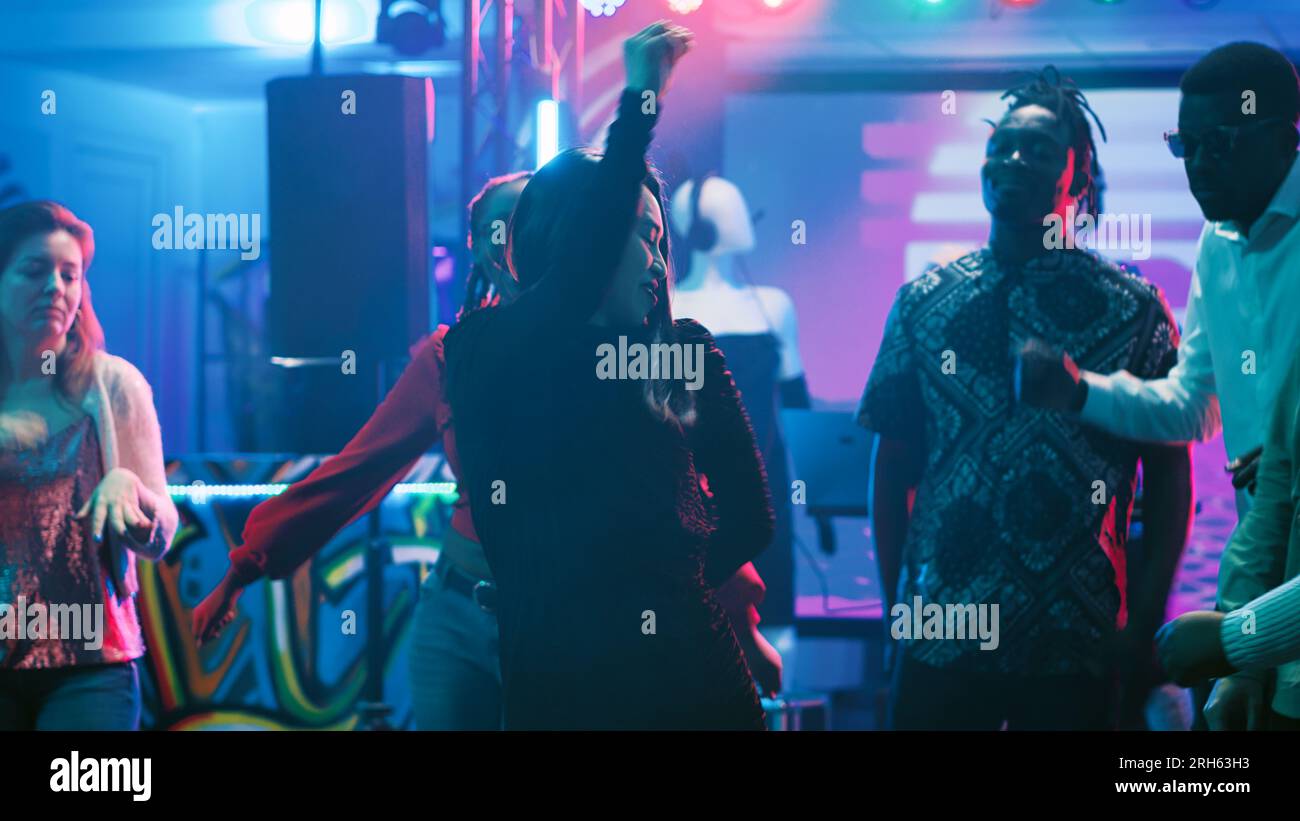 Jeune femme dansant à la discothèque, se sentant joyeuse sur la musique au bar. Groupe d'amis montrant des mouvements de danse funky dans le club, faisant la fête ensemble sur la piste de danse avec des lumières. Prise de vue sur trépied. Banque D'Images