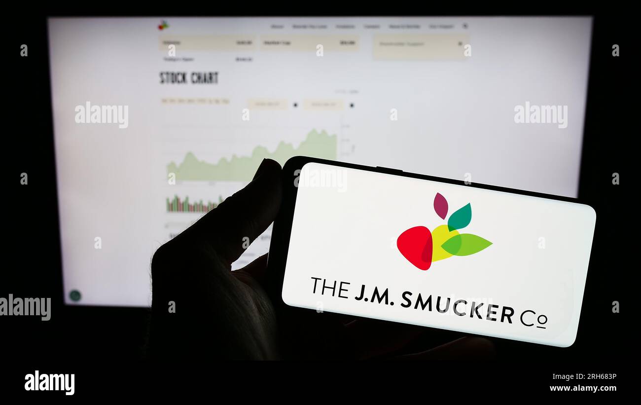 Personne tenant le téléphone mobile avec le logo de l'entreprise alimentaire américaine J.M. Smucker Company sur l'écran en face de la page Web. Concentrez-vous sur l'affichage du téléphone. Banque D'Images