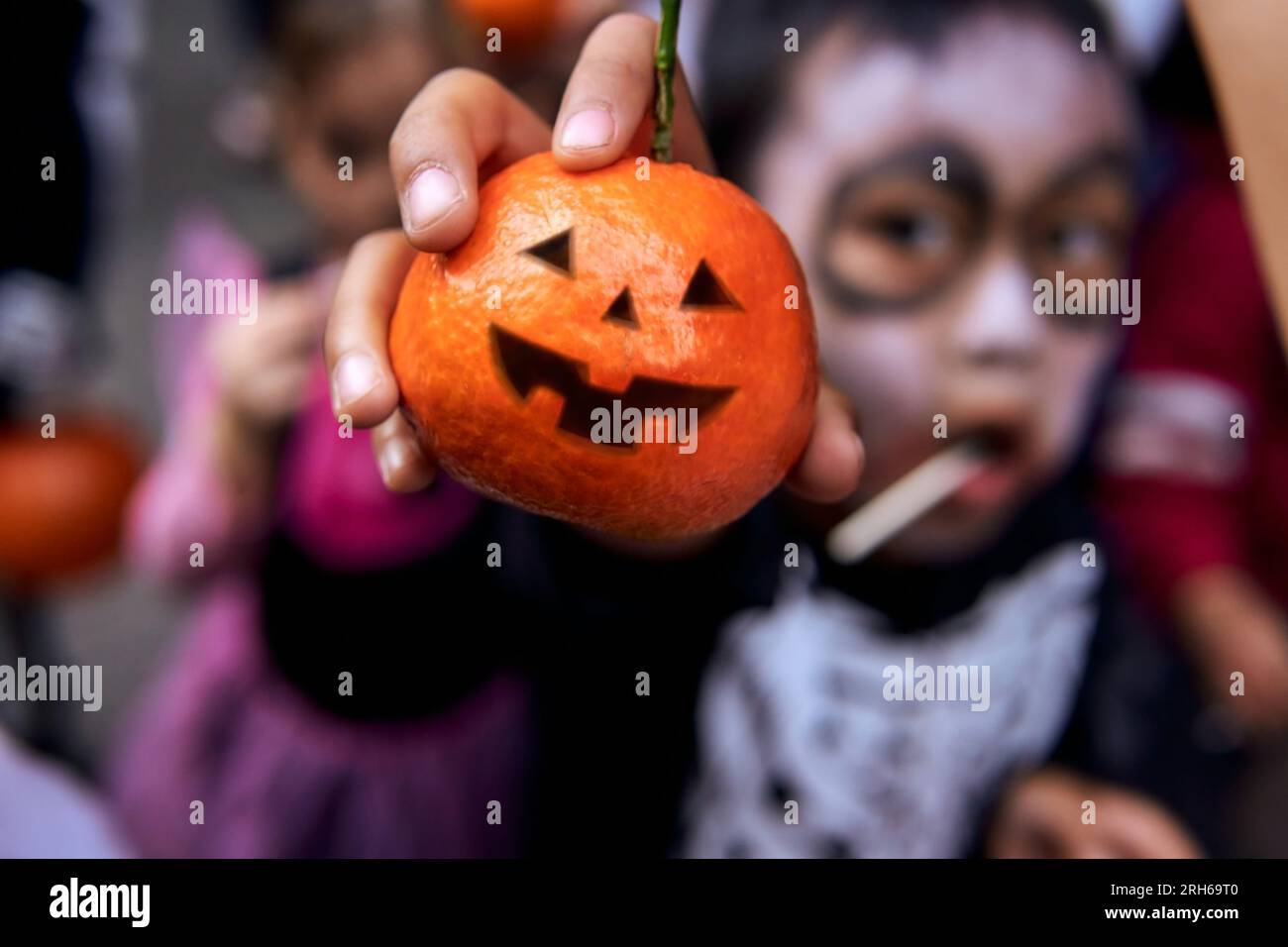 Enfant asiatique en costume de squelette montrant la citrouille mandarine d'halloween comme traitement sain Banque D'Images