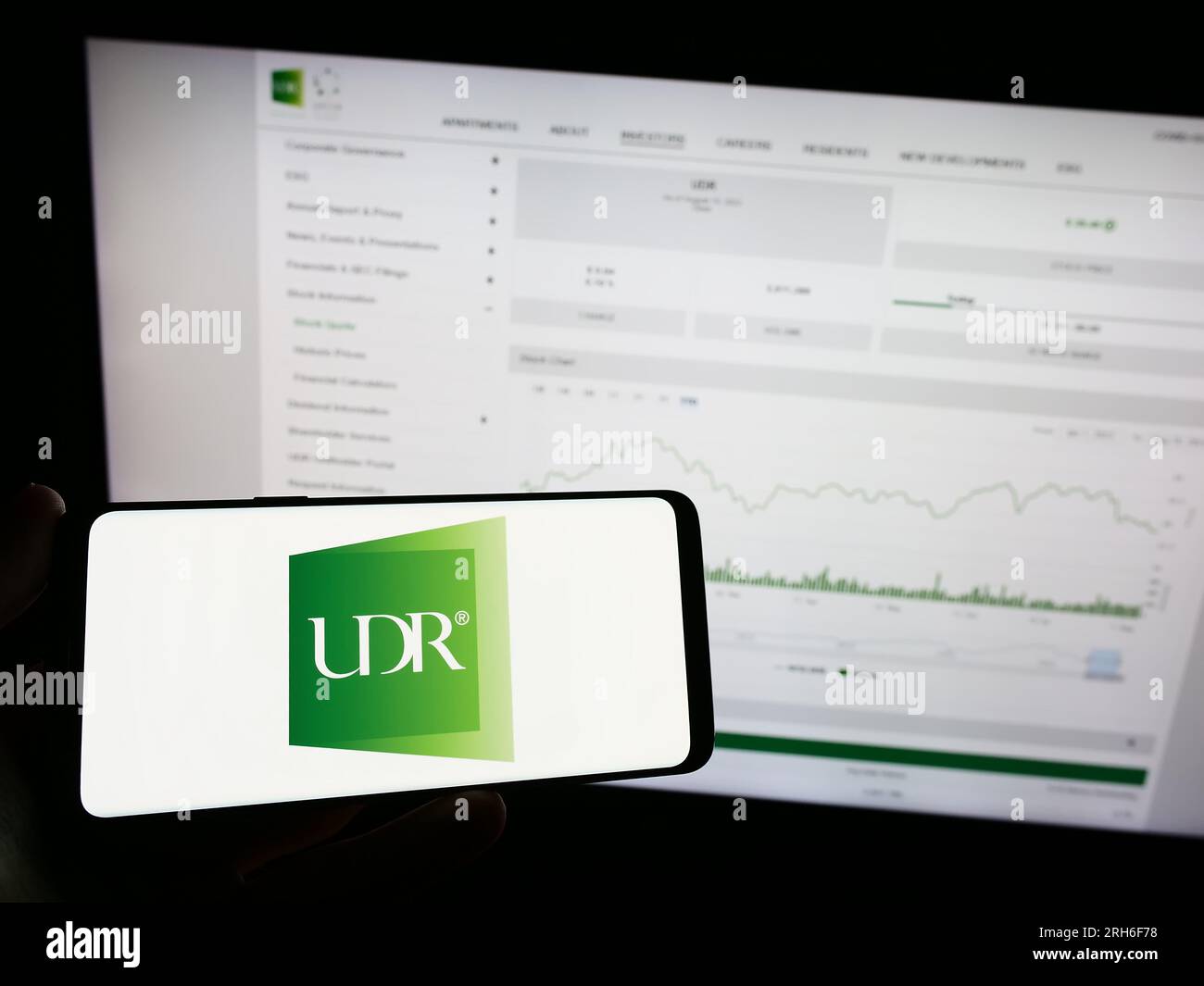 Personne tenant le téléphone mobile avec le logo de la société immobilière américaine UDR Inc. Sur l'écran en face de la page Web d'affaires. Concentrez-vous sur l'affichage du téléphone. Banque D'Images