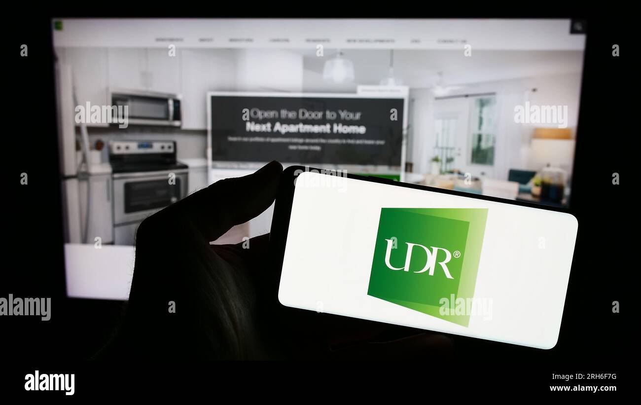 Personne détenant le téléphone portable avec le logo de la société immobilière américaine UDR Inc. Sur l'écran devant la page Web de l'entreprise. Concentrez-vous sur l'affichage du téléphone. Banque D'Images