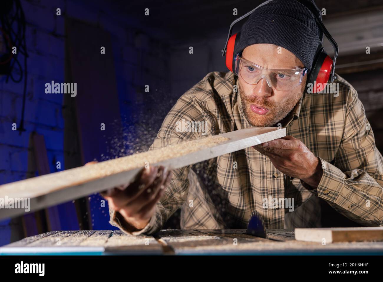 charpentier soufflant de la sciure de bois à partir de planches de bois après la coupe avec scie circulaire. homme travaillant en atelier Banque D'Images