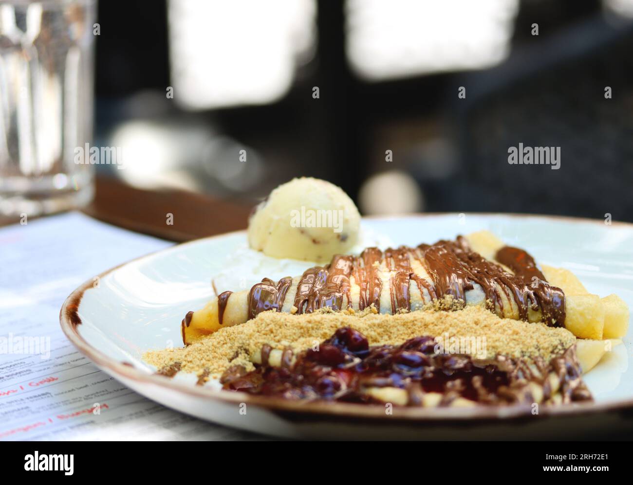 Crêpes à la crème au chocolat, espace de copie. Crêpes à la pâte de chocolat, noisettes, sauce cerise et une boule de glace sur une assiette blanche sur un restaurant Banque D'Images
