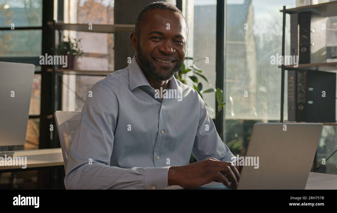 Âgé d'âge moyen mature homme ethnique afro-américain directeur général s'assoit à la société ensoleillée d'agence d'affaires de bureau tapant l'email sur la recherche d'ordinateur portable Banque D'Images