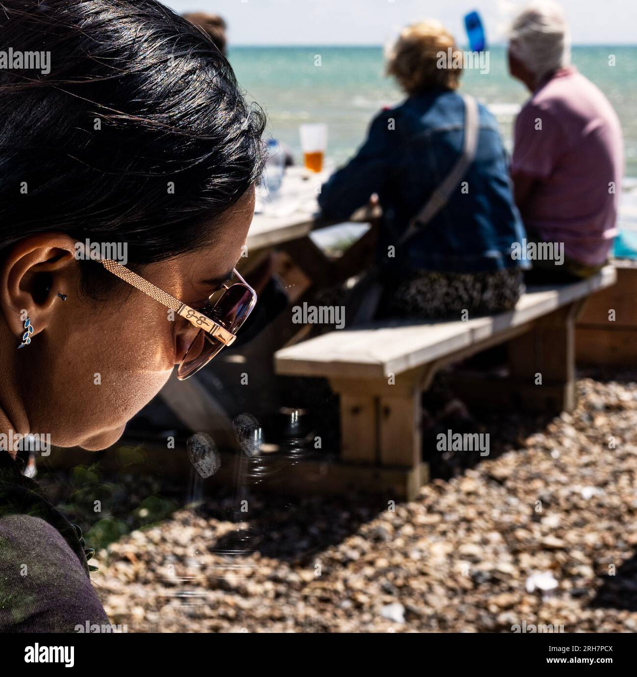 Gros plan d'une jeune femme aux lunettes de soleil assise sur la plage de Littlehampton, West Sussex Banque D'Images