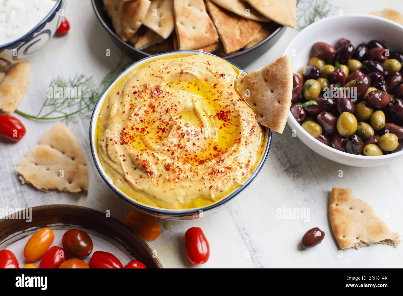 Vue aérienne d'un plateau de mezze de houmous et de pain pita entouré de tomates fraîches, d'olives et de tzatziki végétalien tremper sur une table rustique blanche. Banque D'Images