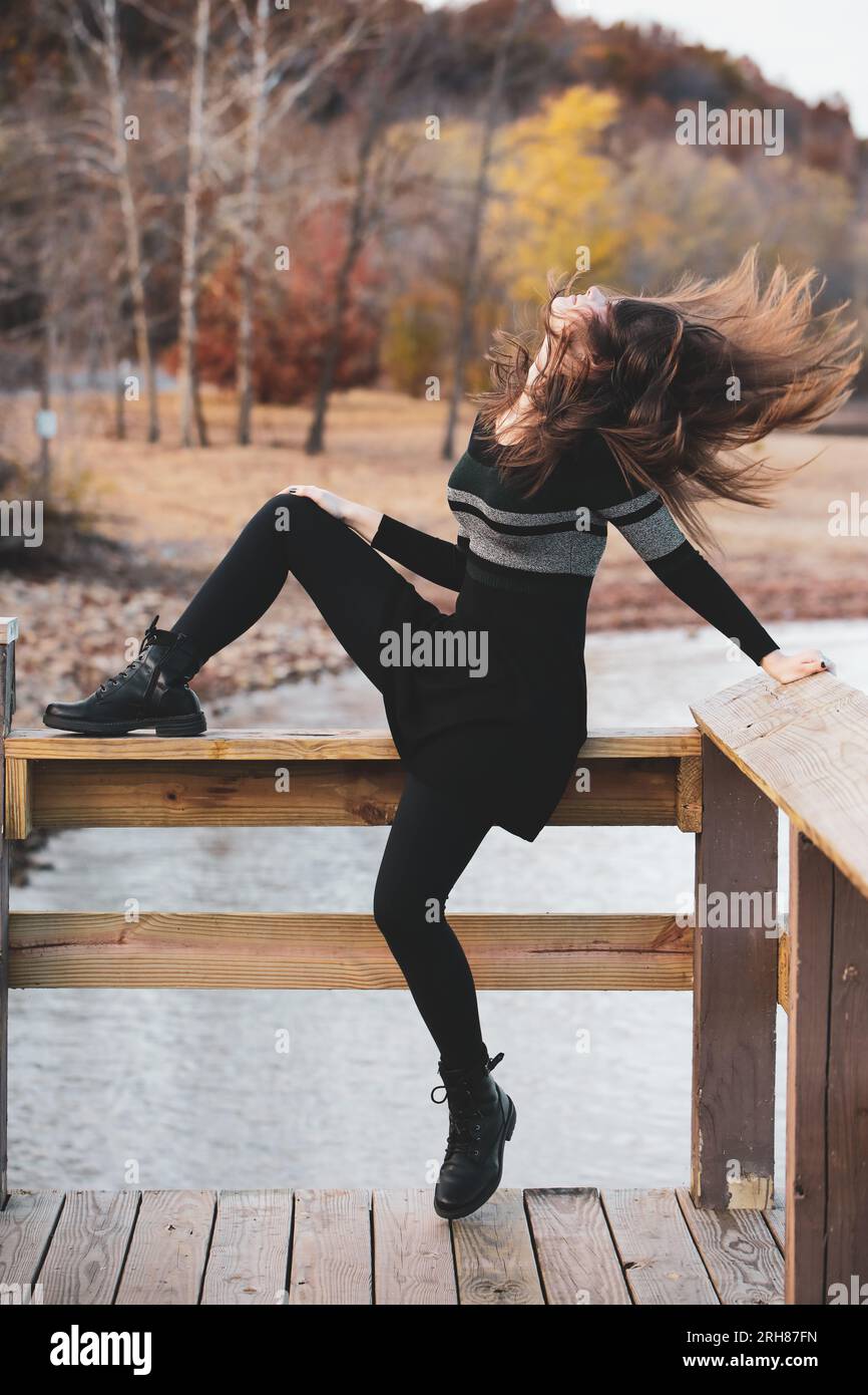 Jeune femme jetant sa tête en arrière avec de longs cheveux volant autour d'elle. Lac et scène d'automne. Banque D'Images