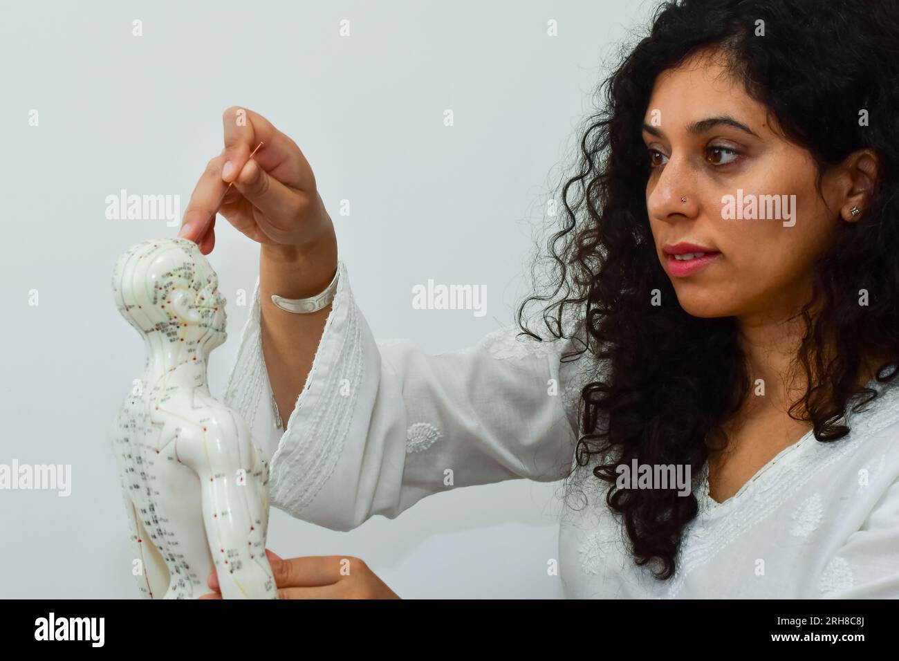 Femme enfonçant une aiguille pour acupuncture dans un mannequin humain. Banque D'Images
