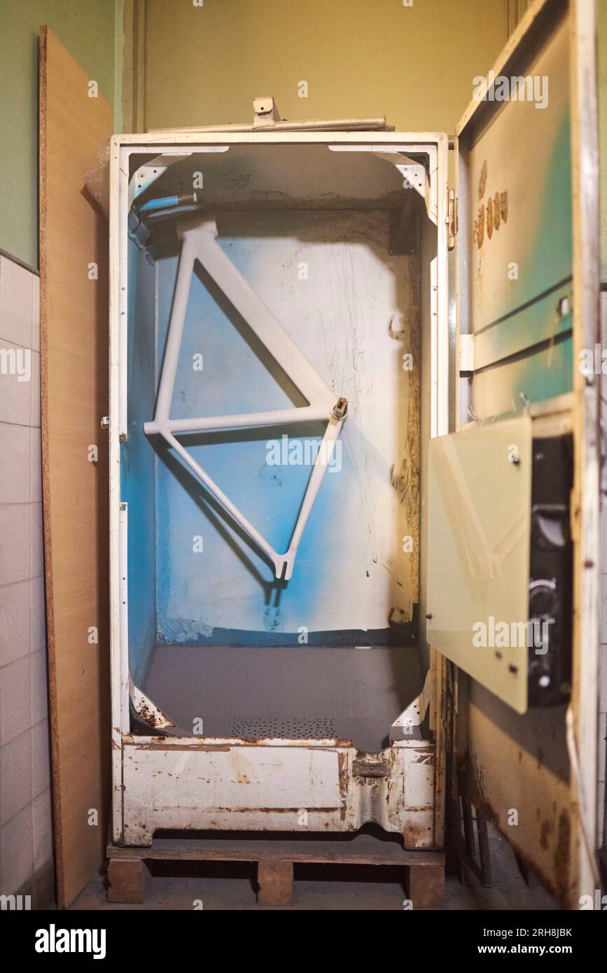 Cadre de vélo fraîchement peint suspendu à l'intérieur de l'étuve de séchage dans l'atelier. Banque D'Images