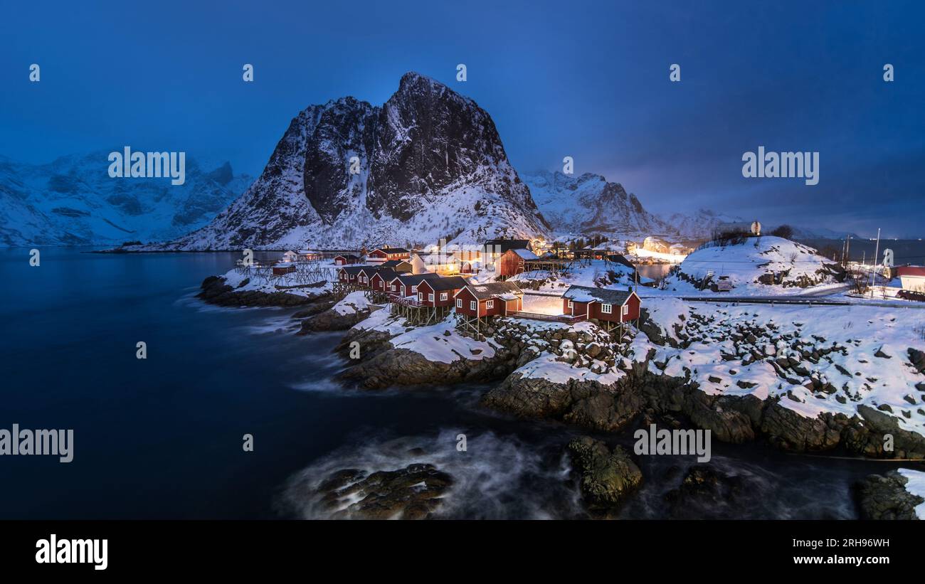 Hamnoy dans des conditions hivernales nuageuses avec des lumières de la ville à l'heure bleue Banque D'Images