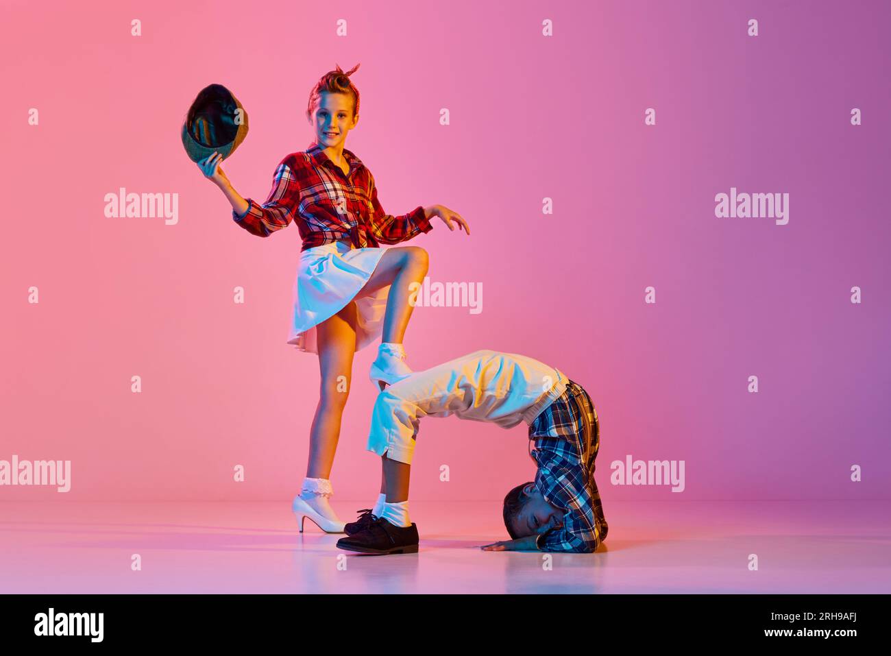 Flexibilité. Enfants élégants et actifs, fille et garçon dans des vêtements de style rétro dansant sur fond de studio rose dans la lumière néon Banque D'Images