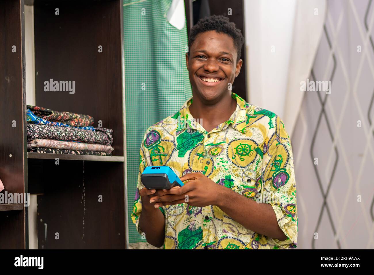 Photo d'un homme africain noir portant du tissu debout à côté d'une armoire en tissu utilisant un terminal de machine pos Banque D'Images