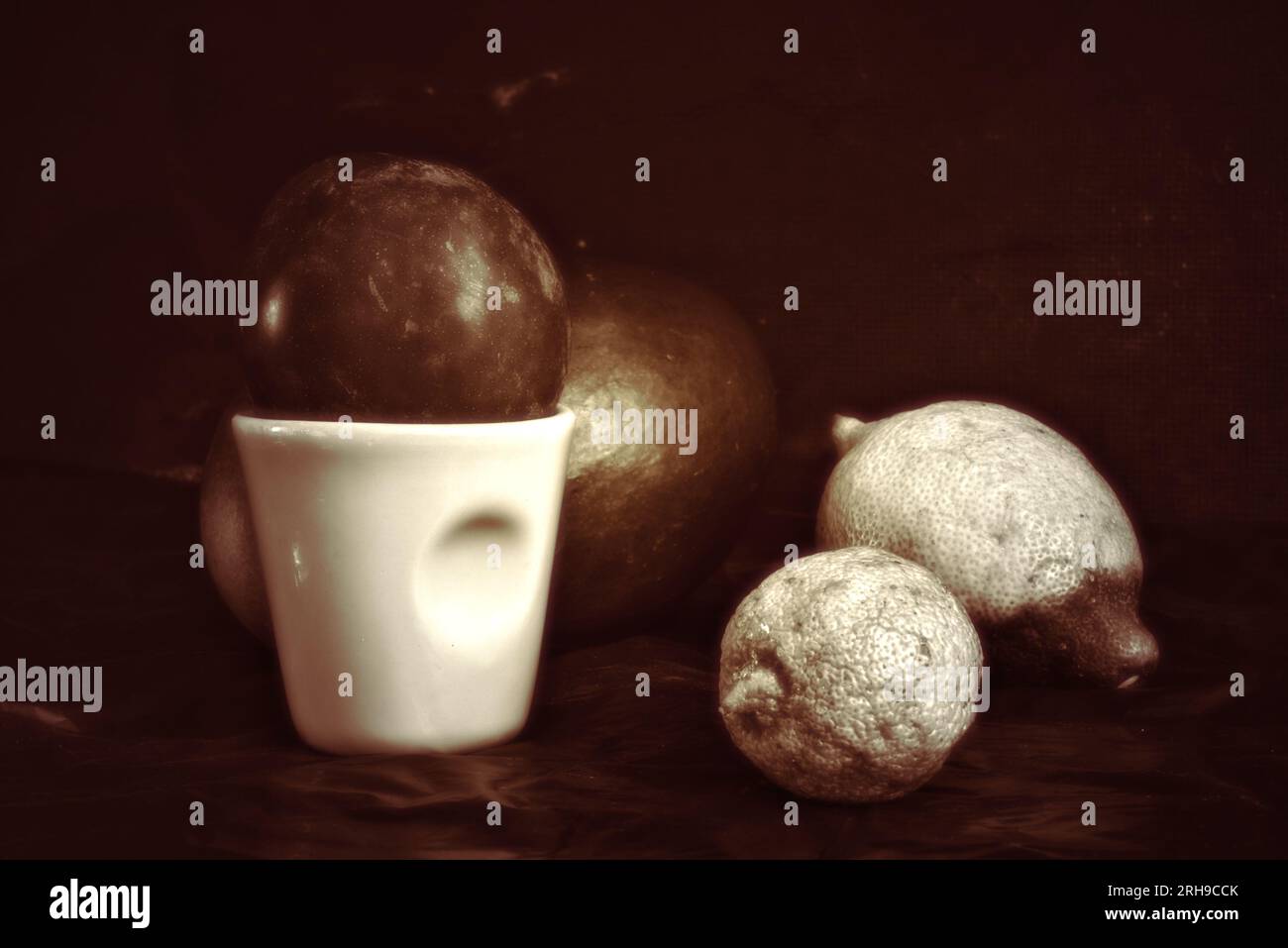 Brune nature morte avec 1 tasse de café, 1 mangues, 2 citrons. Monochrome avec fond sombre (photo studio) Banque D'Images