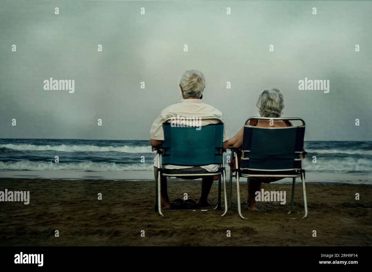 Heureusement pour toujours. Grands-parents romantiques amoureux à la plage. Deux personnes âgées assises à la plage l'une à côté de l'autre profitant d'une journée nuageuse. Banque D'Images