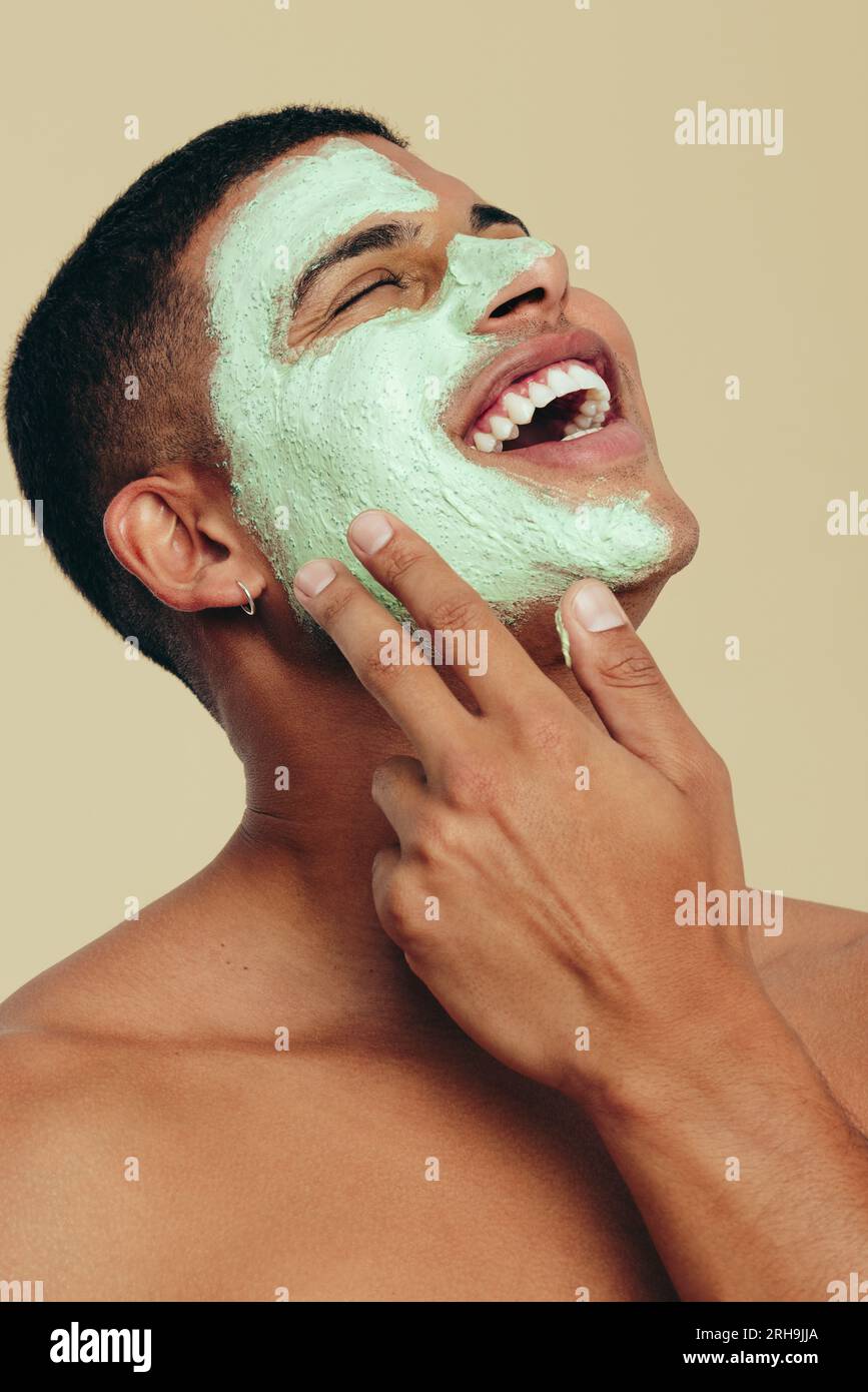Beau jeune homme appréciant sa routine beauté, souriant alors qu'il applique un masque hydratant et hydratant sur sa peau éclatante. Pratique de jeune homme heureux Banque D'Images
