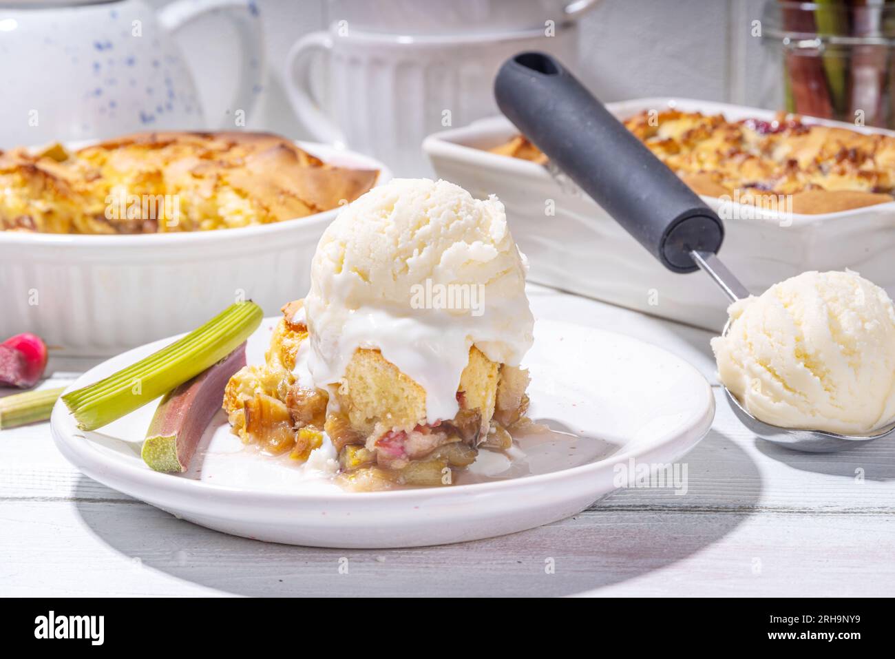 Tarte parée à la framboise aux baies, gâteau maison à l'éponge avec rhubarbe sucrée et fraise, servi avec boule de glace à la vanille, sur un k en bois blanc ensoleillé Banque D'Images