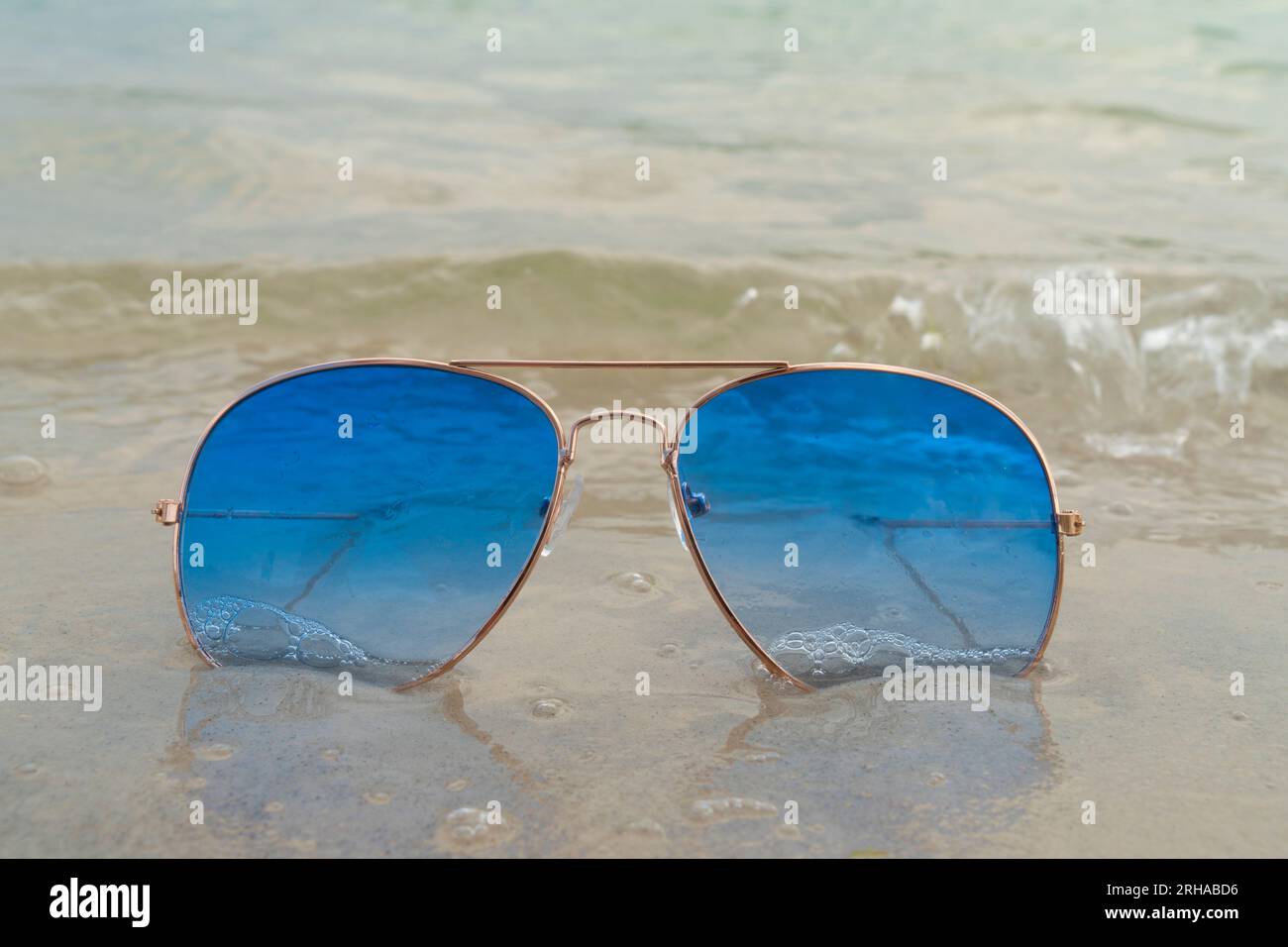 Lunettes de soleil bleues reposent dans le sable sur la plage près de la mer. Vacances d'été, voyage et concept de tourisme. Repos estival. Saison des vacances. Banque D'Images