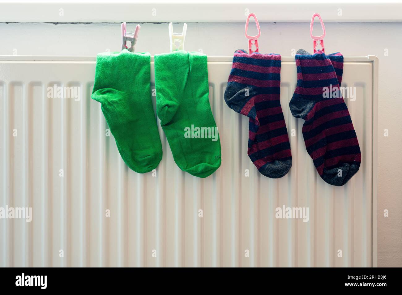 Deux paires de chaussettes colorées vertes et rayées avec pince à linge sur le radiateur blanc après lavage. Logement, économie, thème domestique Banque D'Images