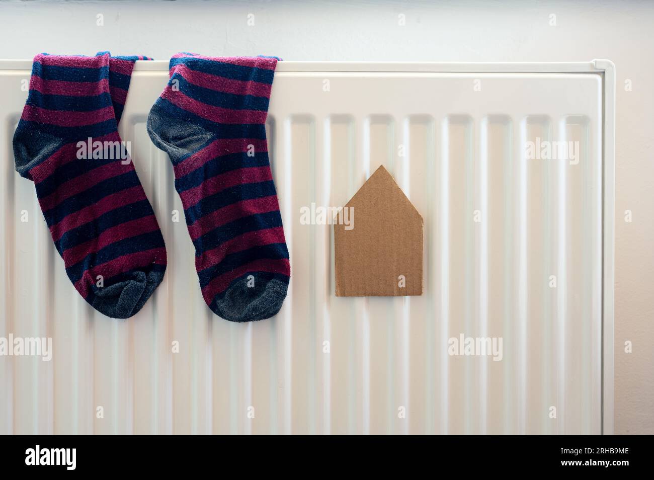 Maison de papier et paire de chaussettes colorées sur le radiateur blanc. Logement, énergie, économie, thème domestique Banque D'Images