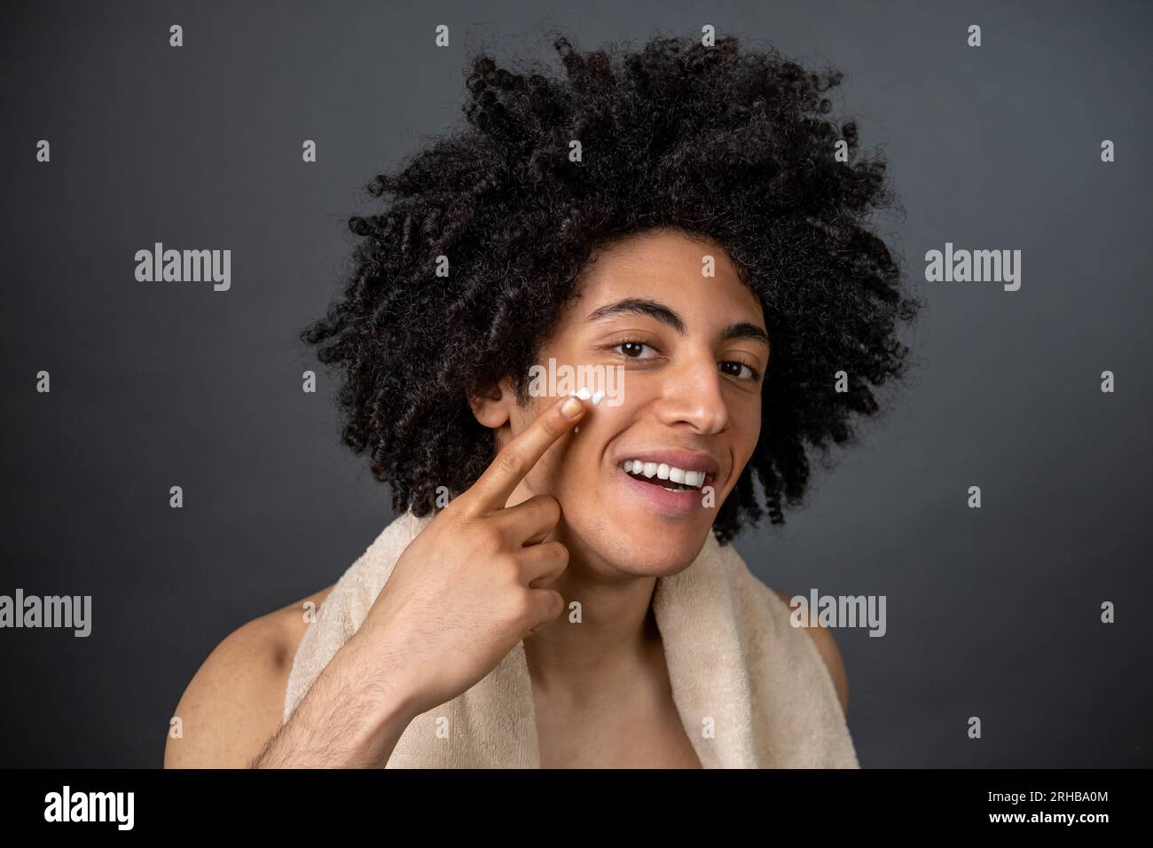 Mec souriant avec une serviette sur le cou appliquant de la crème pour le  visage Photo Stock - Alamy