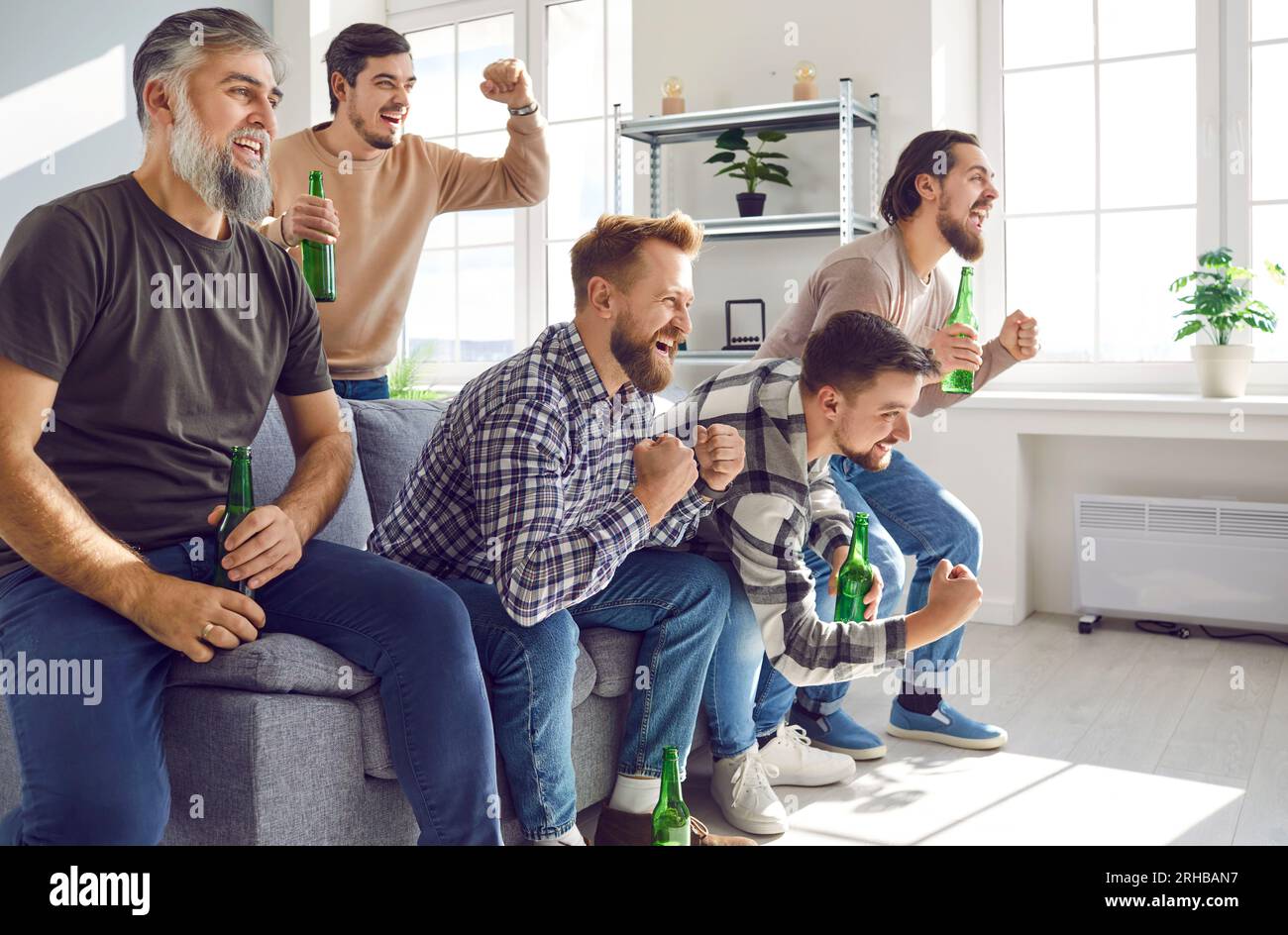 Groupe d'amis excités regardant le match de football à la télévision à la maison avec de la bière. Banque D'Images