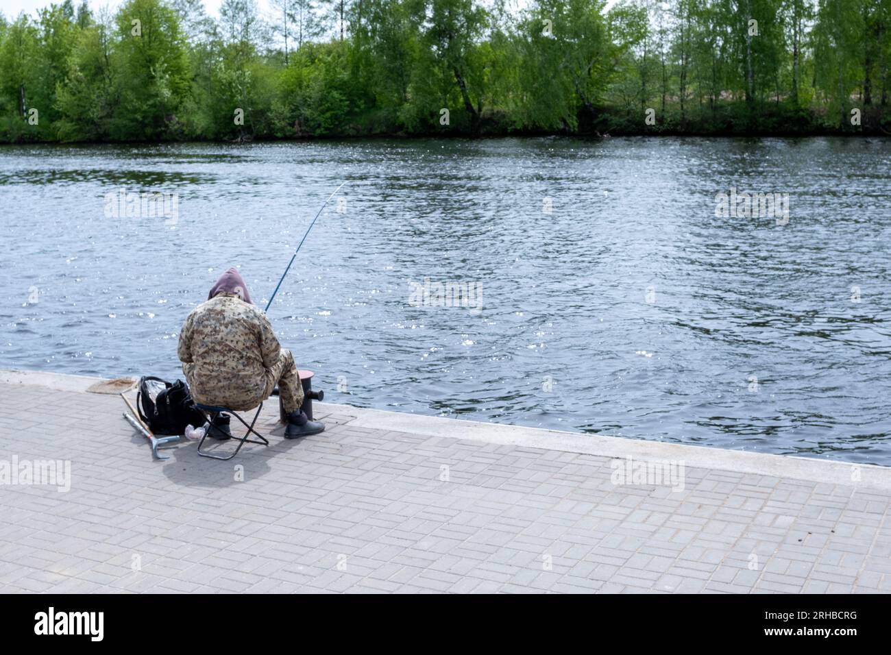 Un pêcheur avec une canne à pêche est assis sur une chaise sur la jetée Banque D'Images