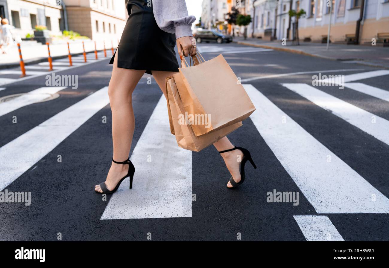 Femme élégante avec des sacs à provisions traversant la route à un passage de zèbre Banque D'Images