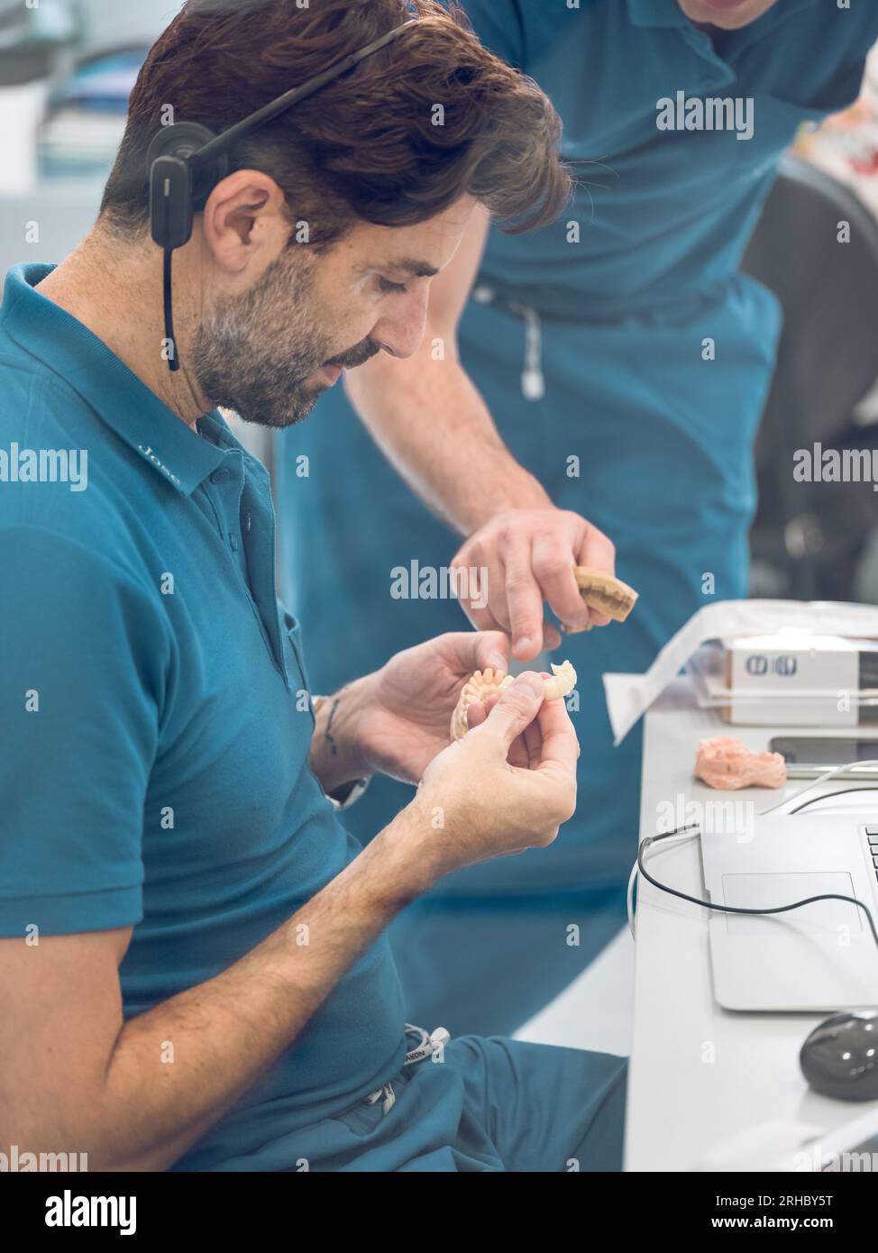 Vue latérale des spécialistes masculins de l'examen uniforme des prothèses dentaires artificielles en céramique dans le laboratoire dentaire moderne Banque D'Images