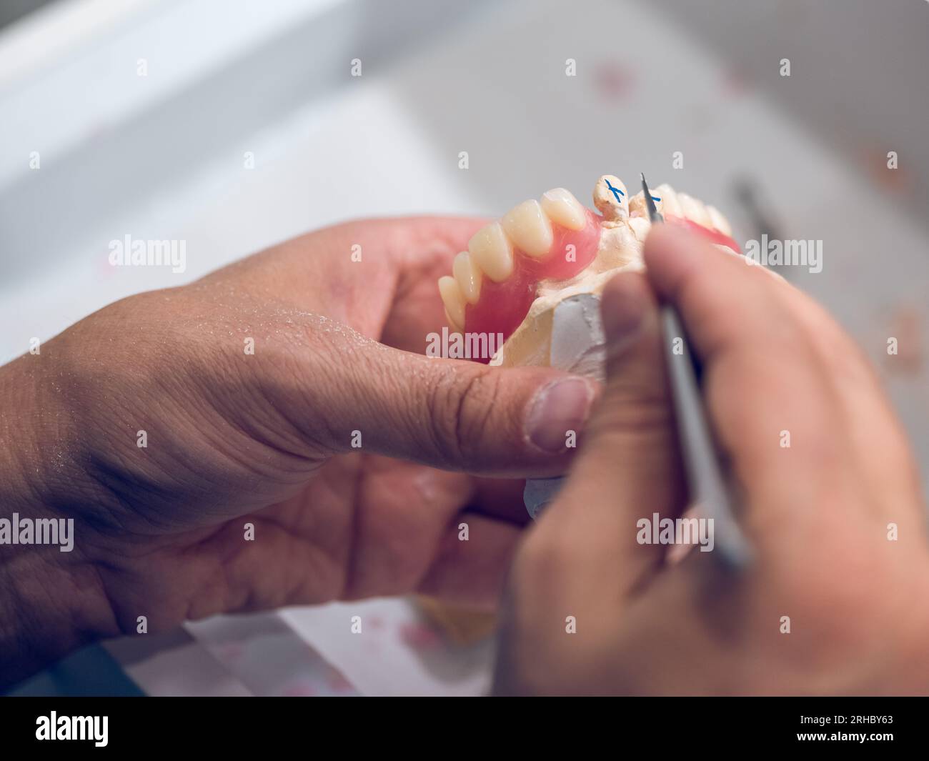 Du haut de la récolte, un spécialiste dentaire masculin méconnaissable sculptant des dents artificielles en céramique à l'aide d'un outil pointu métallique tout en travaillant dans un laboratoire dentaire Banque D'Images
