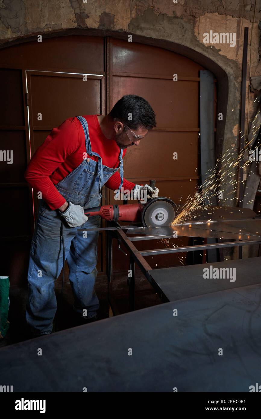 Travailleur masculin dans les lunettes de protection et les gants coupant le fer sur la rampe en métal dans l'atelier professionnel Banque D'Images