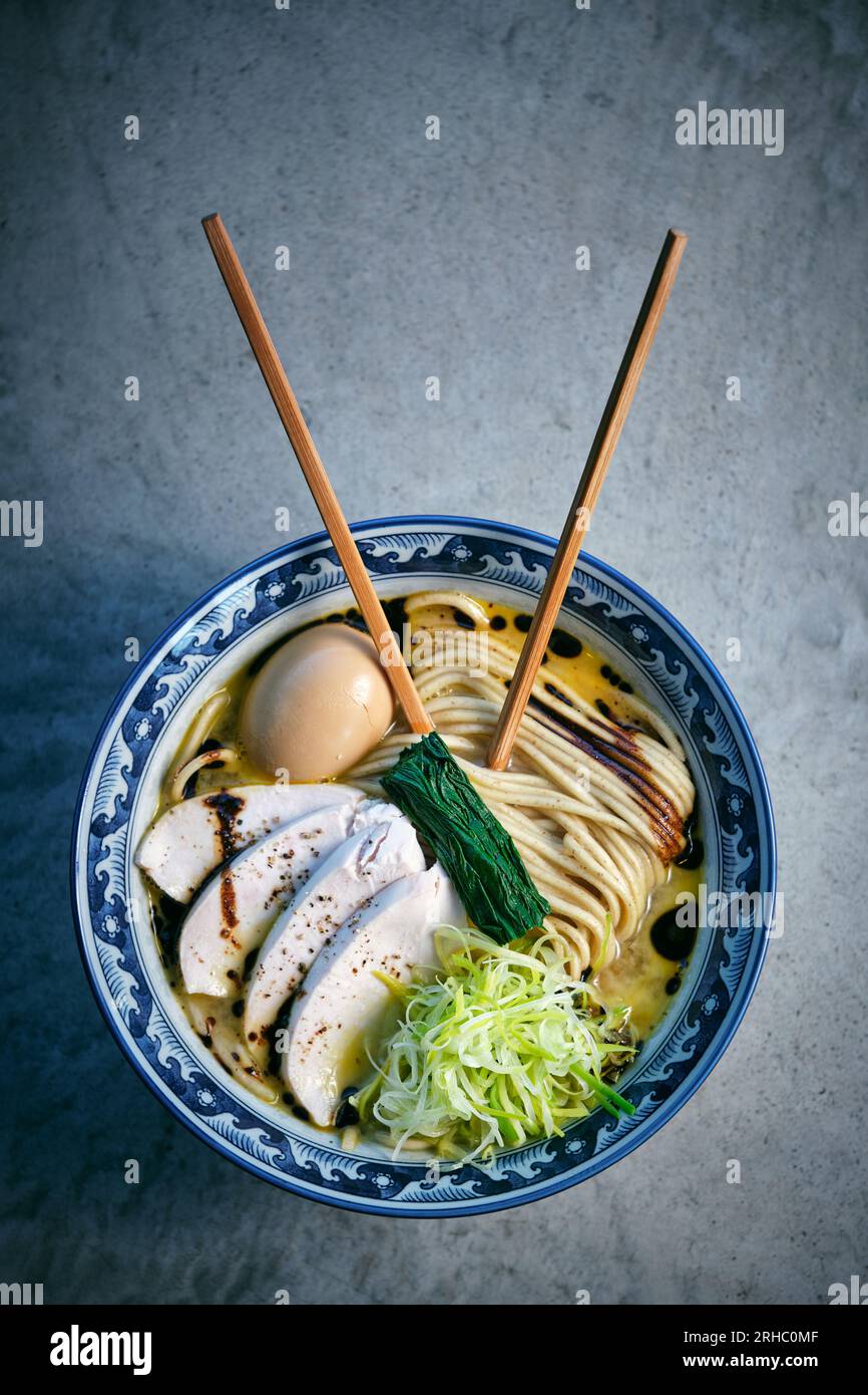 Vue de dessus d'une délicieuse soupe de nouilles japonaises avec des légumes frais et des œufs durs dans un bouillon avec des baguettes sur fond gris Banque D'Images
