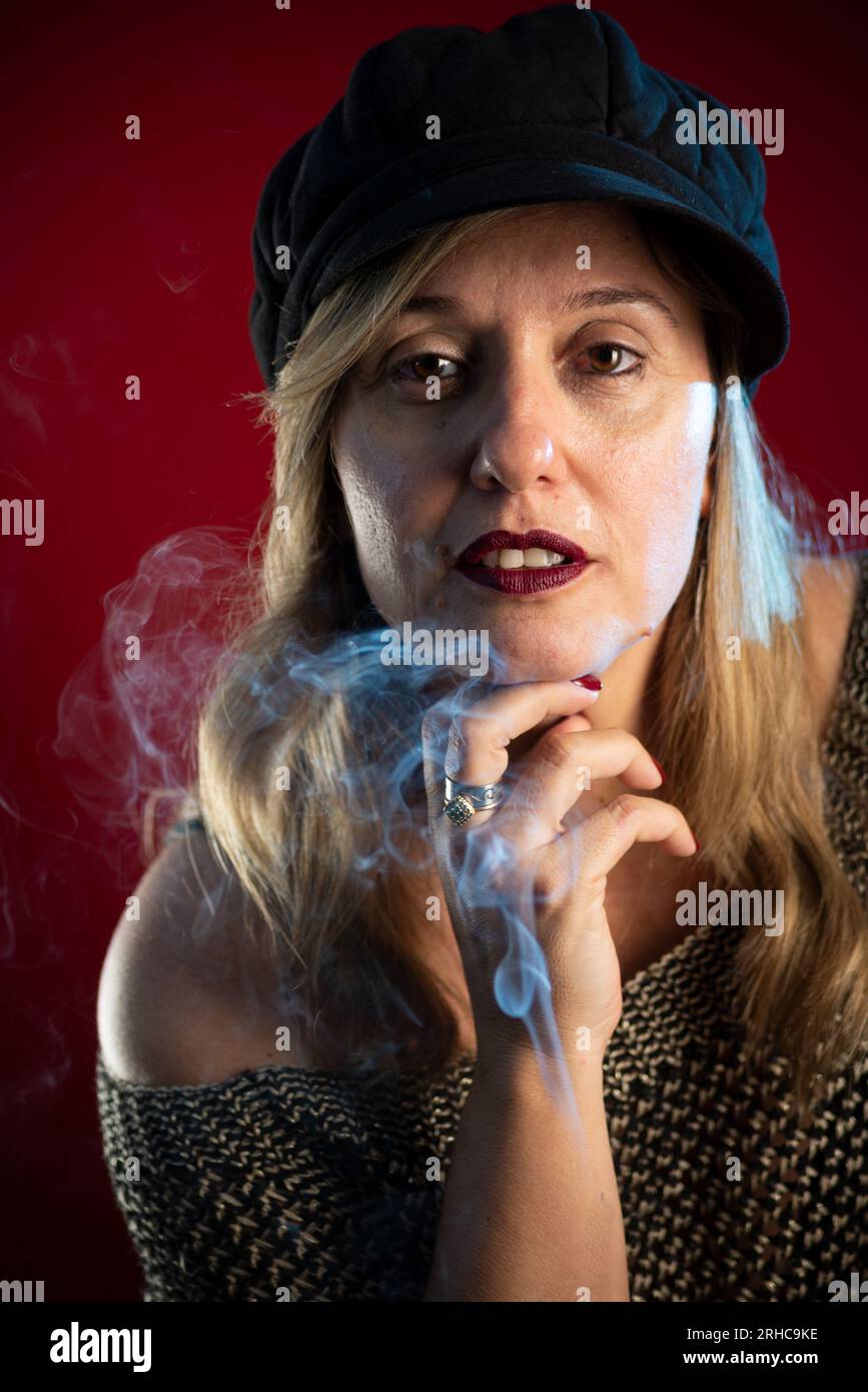 Belle femme portant un béret noir avec la main sur le menton. Fumée d'encens tout autour. Isolé sur fond rouge. Banque D'Images