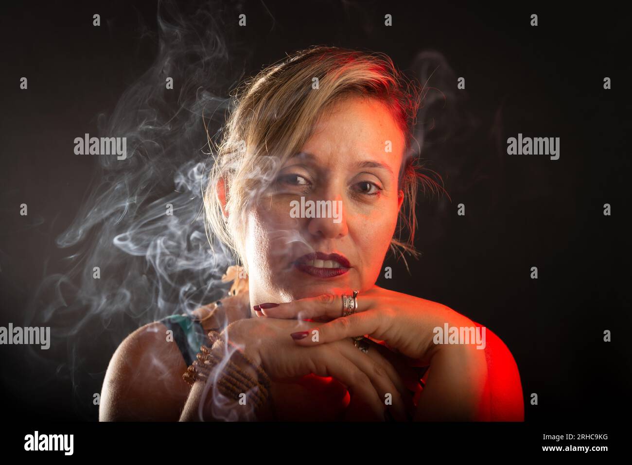 Belle et belle femme calme regardant la caméra avec ses mains sur son visage. Fumée d'Encens tout autour. Portrait de studio. Isolé sur un b noir Banque D'Images