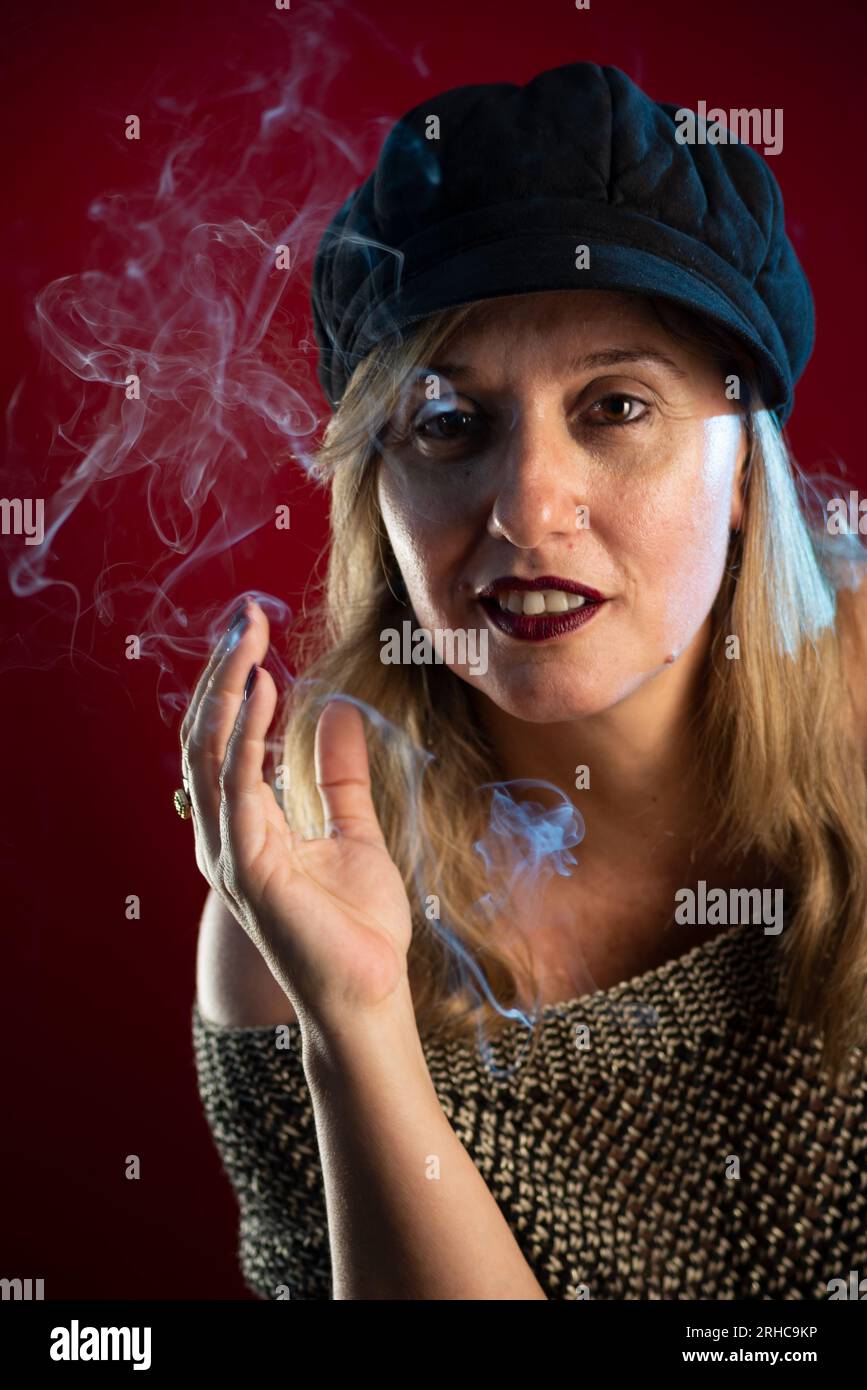 Femme attrayante et confiante portant un béret noir. Fumée d'Encens tout autour. Portrait de studio sur fond rouge. Banque D'Images