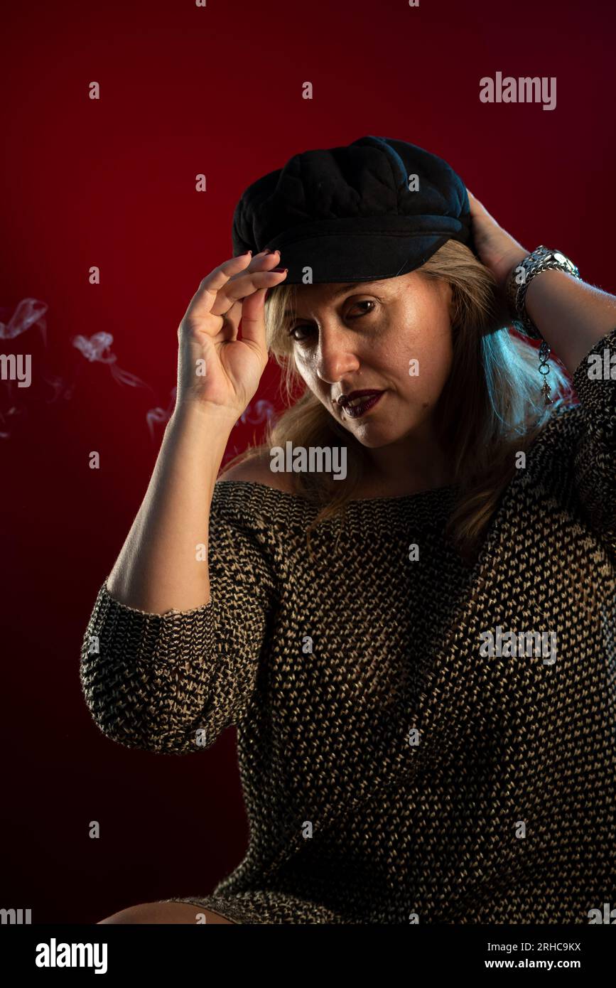 Portrait de studio d'une femme attrayante et belle tenant un béret noir sur sa tête. Fumée d'encens tout autour. Isolé sur fond rouge. Banque D'Images